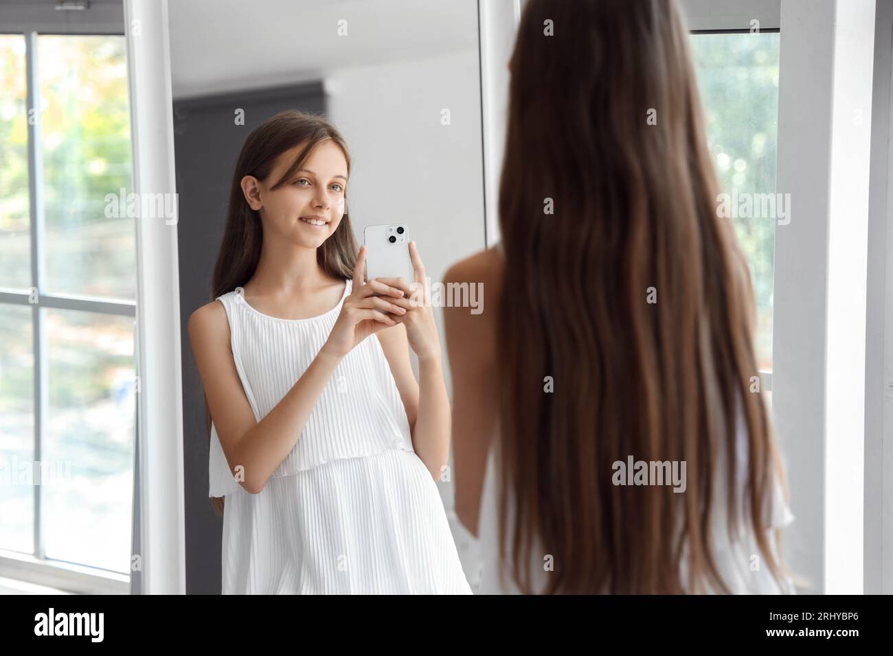 Happy little girl with mobile phone taking selfie in front of mirror at home Stock Photo