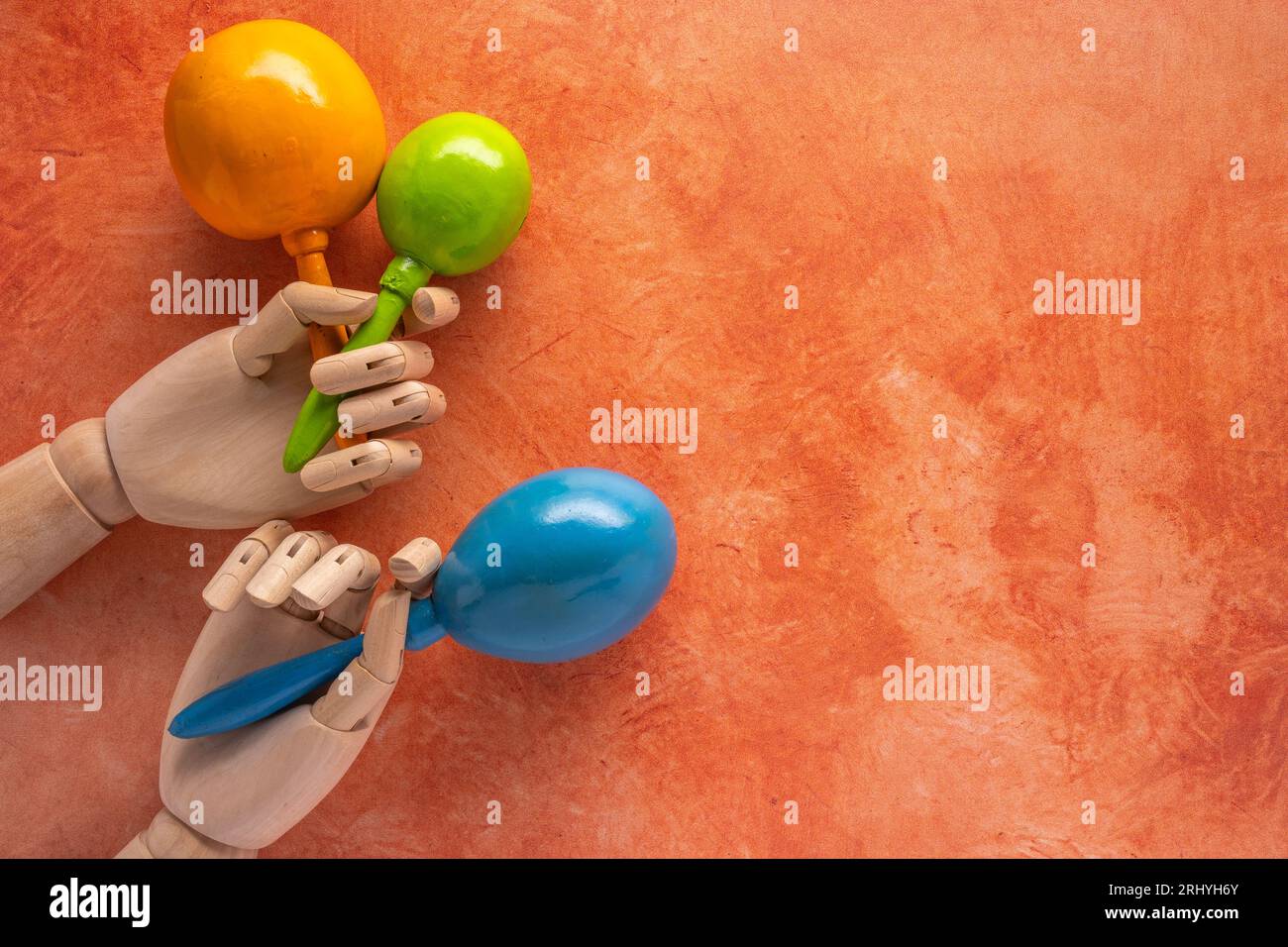 bright festive musical theme with yellow, green and blue maracas in wooden hands on a mottled orange background Stock Photo
