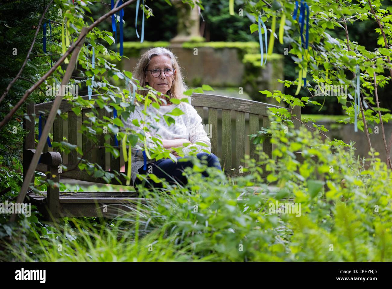 Cologne, Germany. 18th Aug, 2023. Annegret Fleischel sits on a bench at her son's grave at Melaten Cemetery. The 70-year-old spends many hours on a bench at her son's grave. This summer, Cologne has a topic that sets tempers racing: should 'wild benches' be removed from the Melaten cemetery for celebrities, or would that be heartless? (to dpa KORR 'The great Cologne cemetery bench debate' from 20.08.2023) Credit: Rolf Vennenbernd/dpa/Alamy Live News Stock Photo