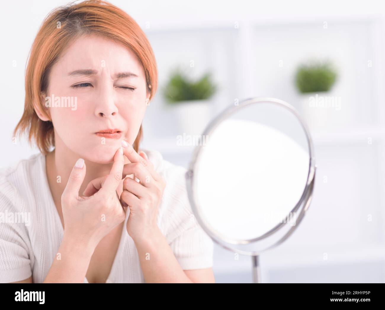 Young woman squeezing pimple spot for removing from face. Stock Photo