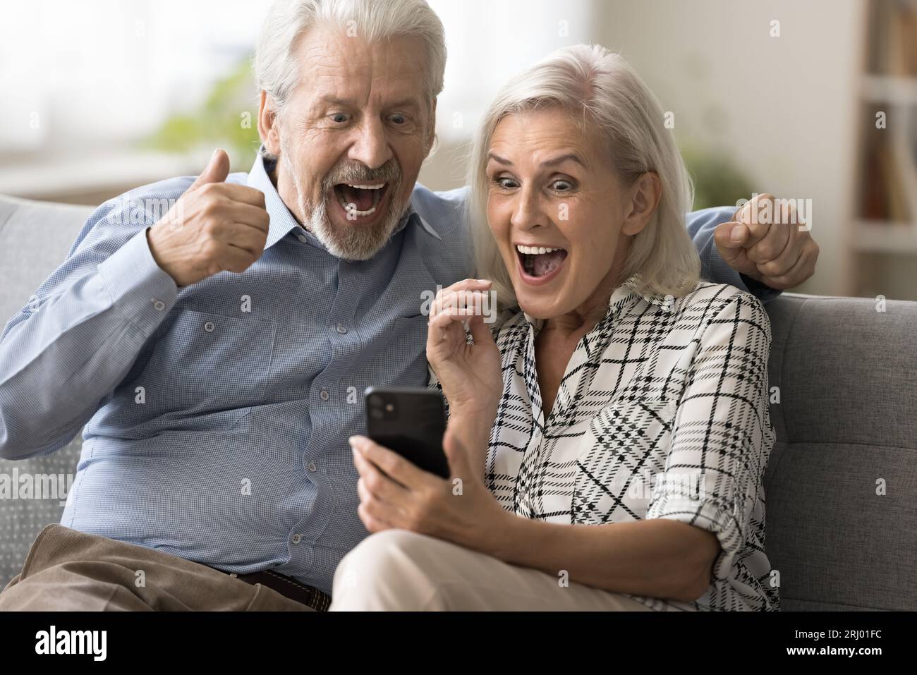 Excited surprised retired couple holding mobile phone Stock Photo