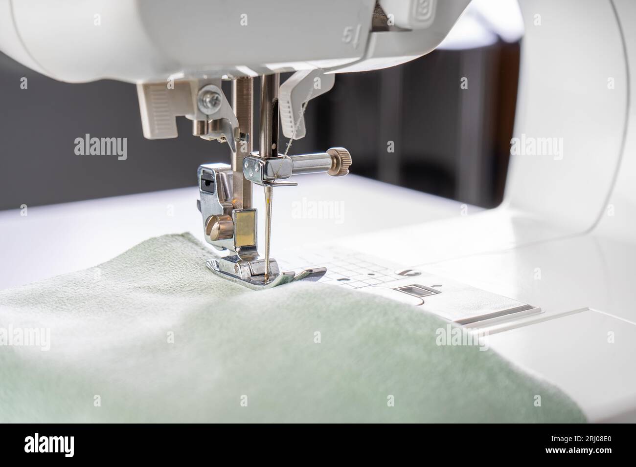 Modern sewing machine presser foot with green fabric and thread, closeup, macro. Sewing process clothes, curtains, upholstery. Business, hobby, handma Stock Photo