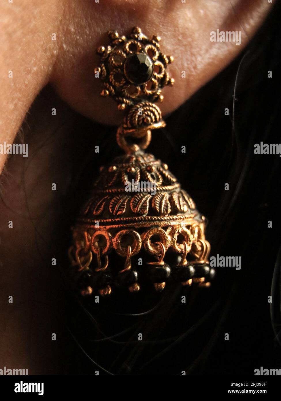 vintage inidan designer gold plated jhumki earring ornament with detailed antique design in closeup on a woman's ear Stock Photo