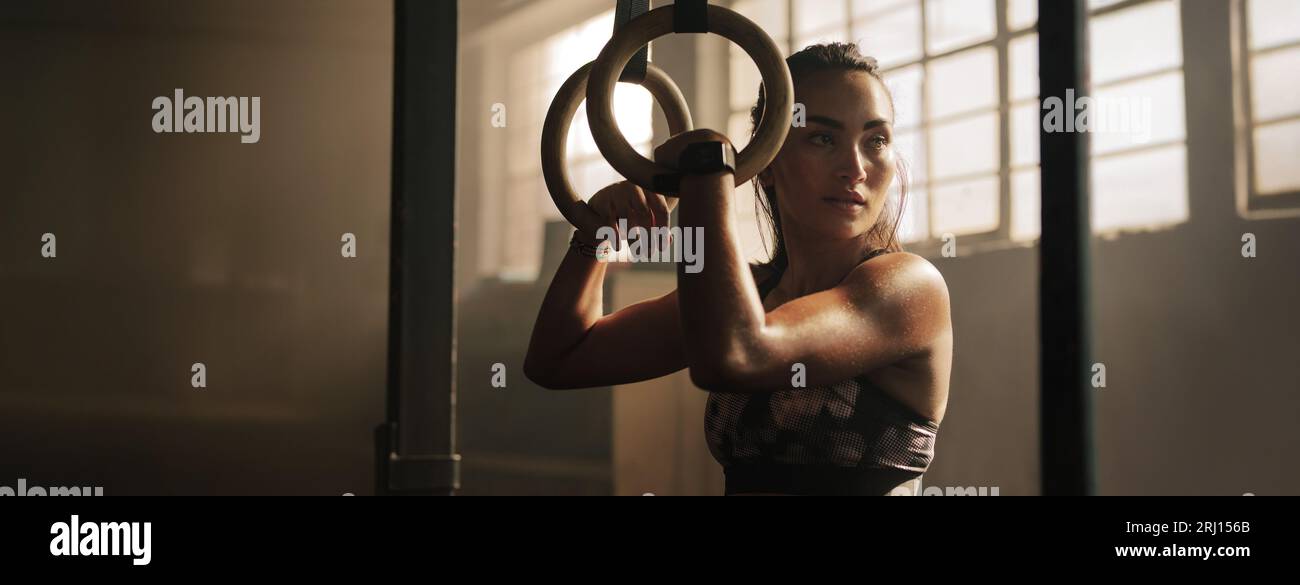Young woman taking a break to catch her breath after a grueling workout on gymnast rings. Female athlete focusing on her fitness routine and training Stock Photo