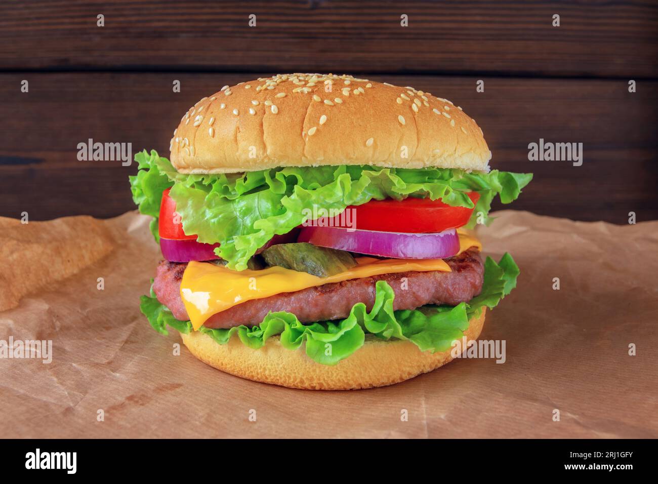 Hamburger or burger with patty of ground beef meat, cheese, lettuce, tomato, onion,  pickles and bun with sesame seeds. Tasty colorful sandwich on the Stock Photo