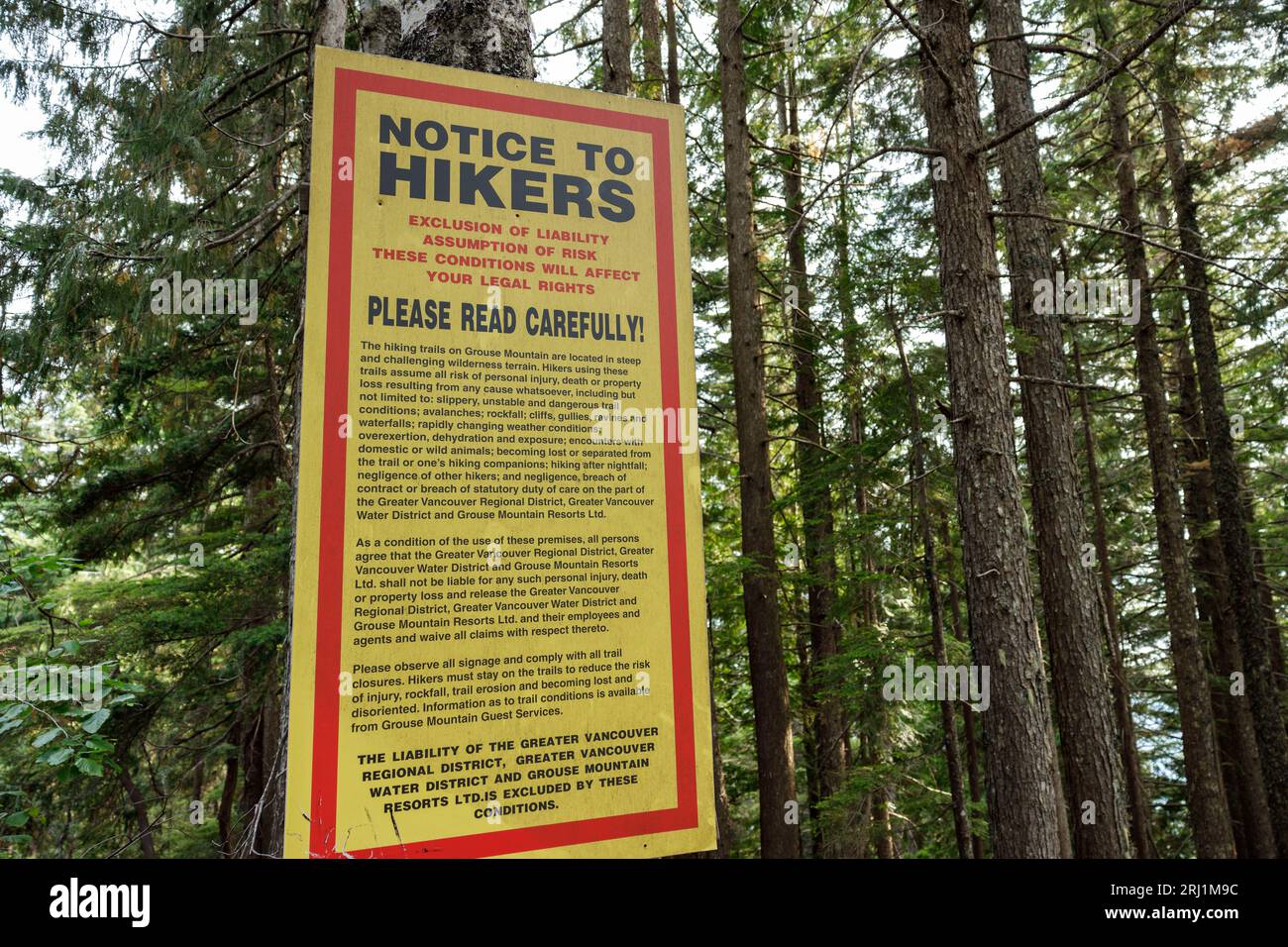 View of a warning sign on the Grouse Grind Trail in Vancouver emphasizing exclusion of liability and assumption of risk. These conditions may impact y Stock Photo