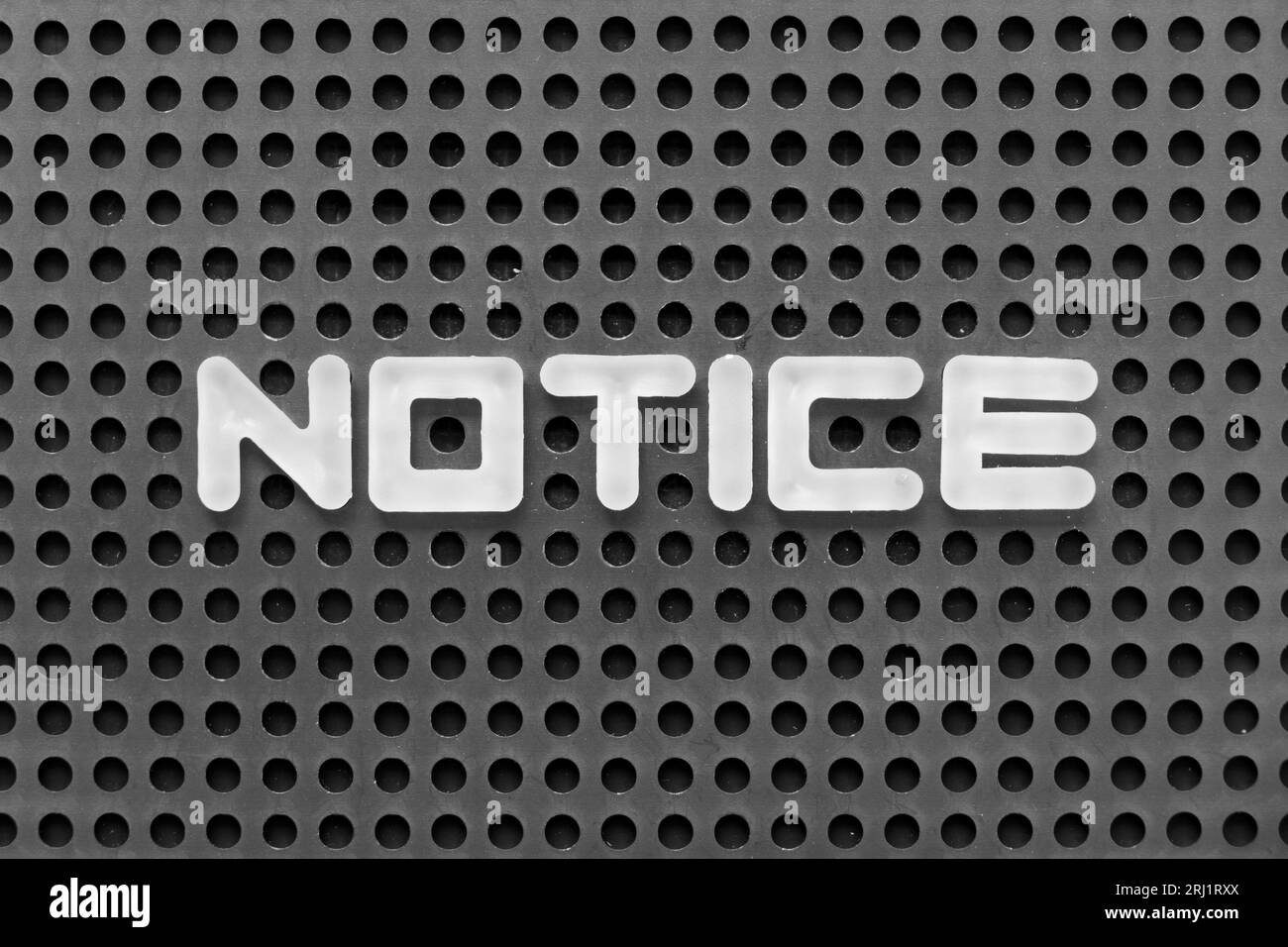 White alphabet letter in word notice on black pegboard background Stock