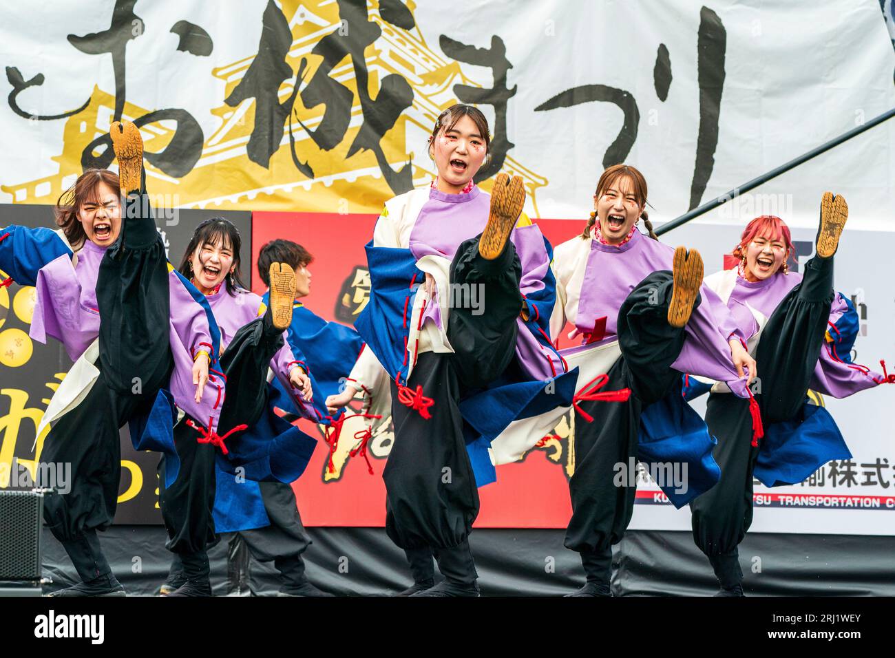 Japanese teenage women Yosakoi dance team in yukata on an open-air stage dancing and kicking their legs up at the Kumamoto Kyusyu Gassai festival. Stock Photo