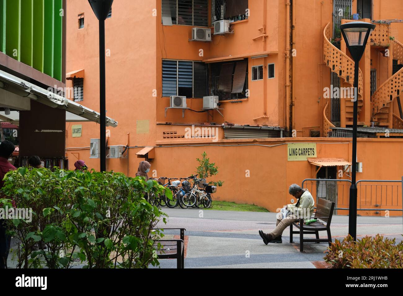 Older man sits on bench near colourful buildings in Singapore's Geylang district. 21/08/2022 Stock Photo