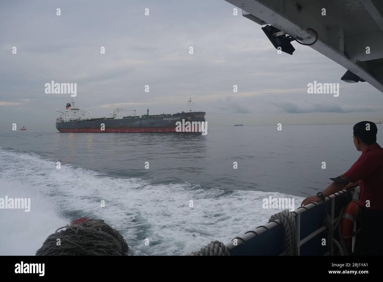 A man on a ferry from Desaru in Malaysia to Singapore looks at a tanker in the Strait of Malacca, one of the world's busiest shipping lanes Stock Photo