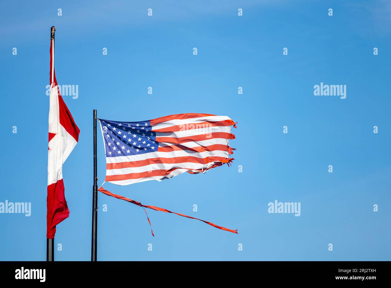 A Weathered and Torn American Flag blowing in the wind beside a Canadian Flag. Stock Photo