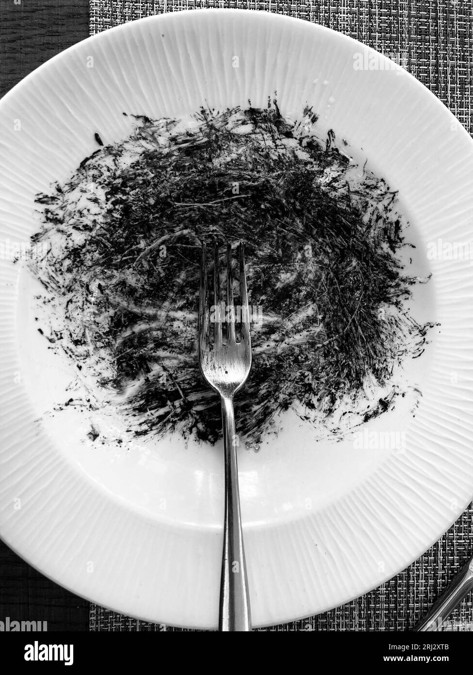 A fork lying on a squid ink splattered dinning plate in black and white Stock Photo