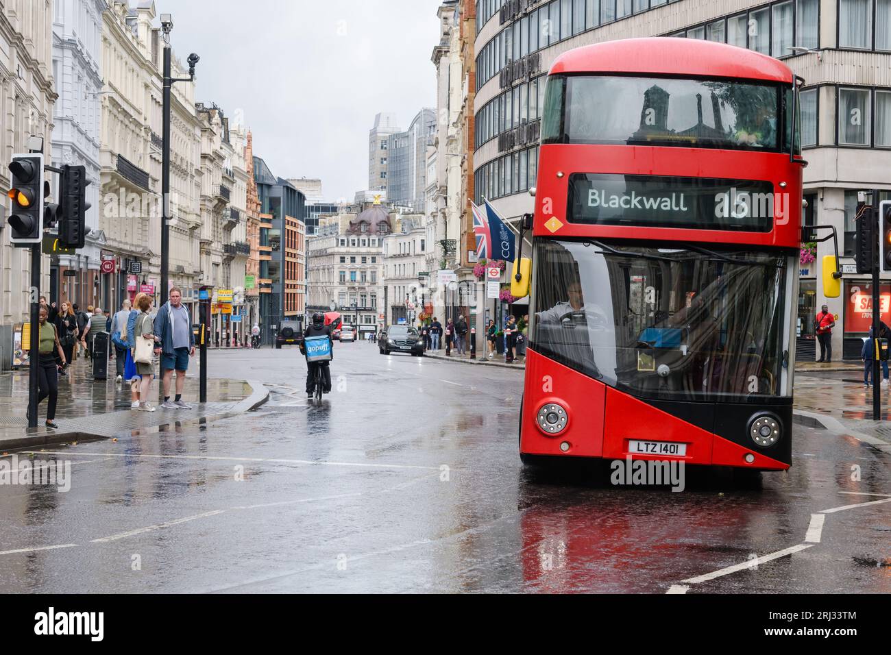 London, UK - July 30, 2023; Red double decker bus leans into curve on wet Ludgate Hill in City of London with pedestrians Stock Photo