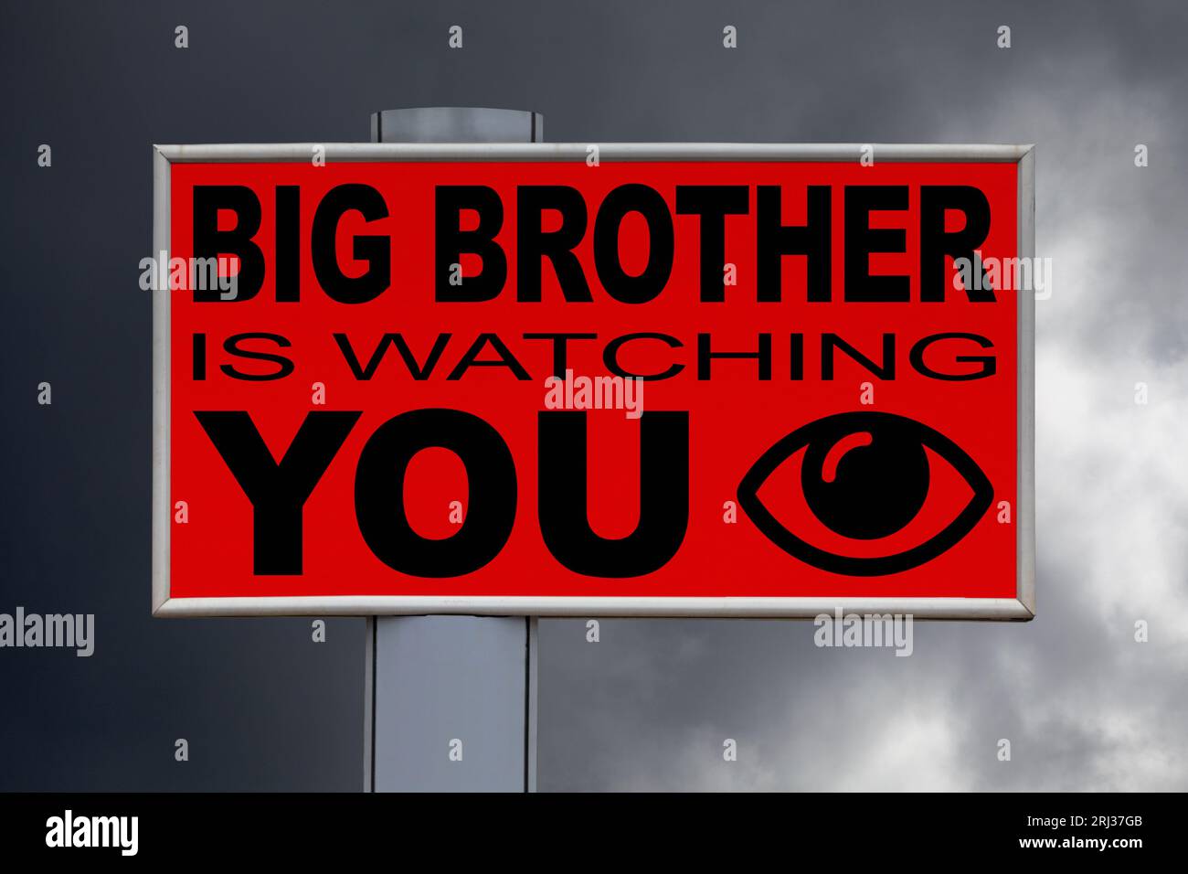 Close-up on a red billboard against a cloudy sky with the message 'Big Brother is watching you' written in the middle next to an eye icon. Stock Photo