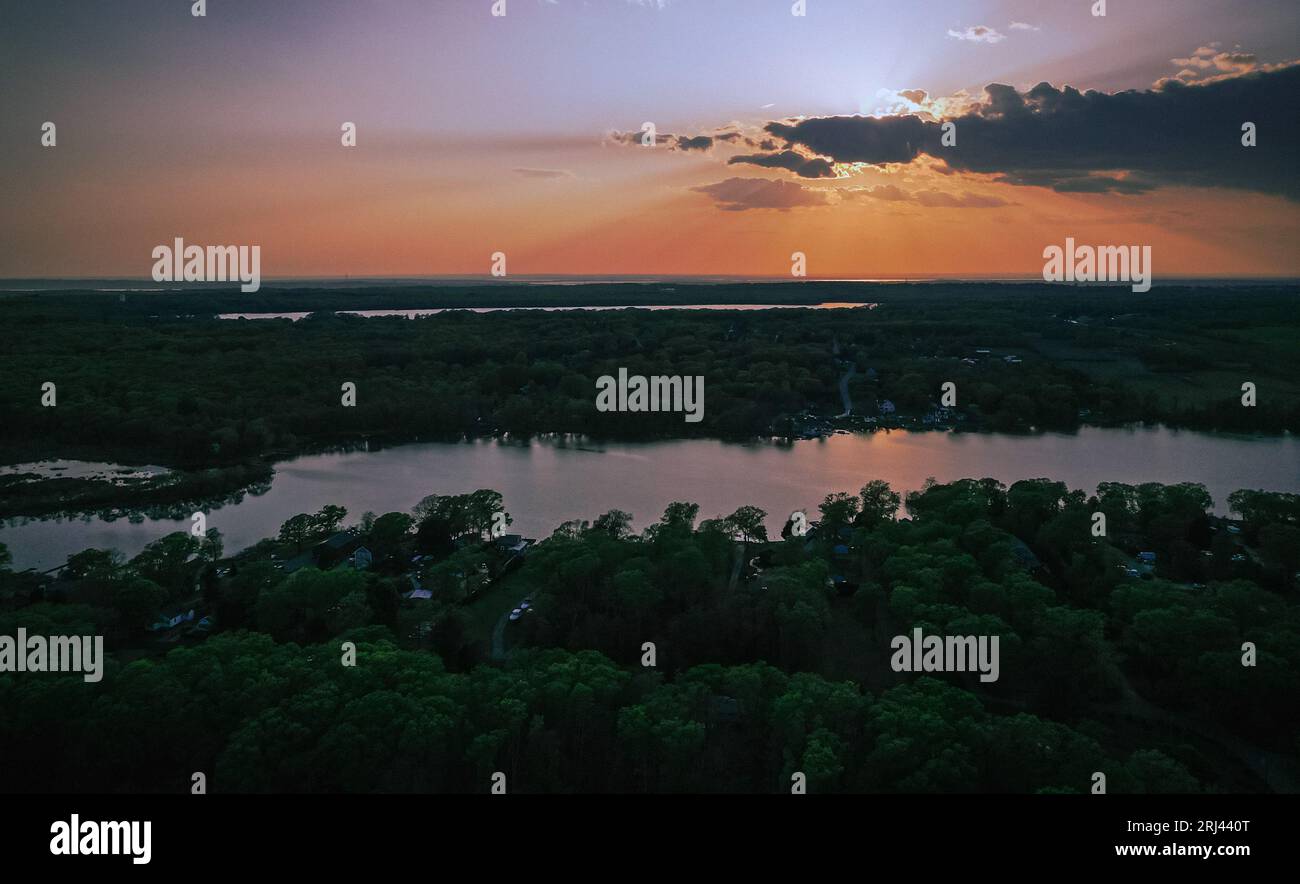 A beautiful sunset illuminates a tranquil lake surrounded by lush trees ...