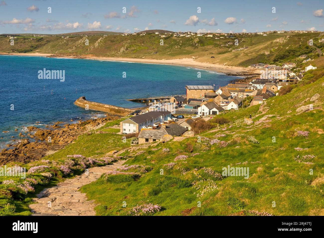 Sennen Cove, near Land's End, Cornwall, on a sunny spring evening, with sea thrift in bloom on the hillside. The path is the start of the walk to Land Stock Photo