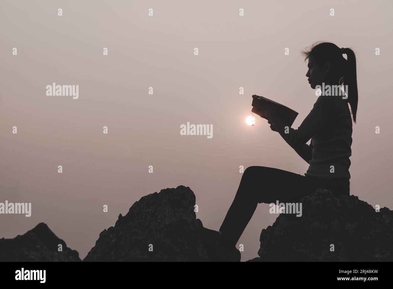 Women standing holding holy  bible for worshipping God at sunset background, Pray to the god, christian silhouette concept. Stock Photo