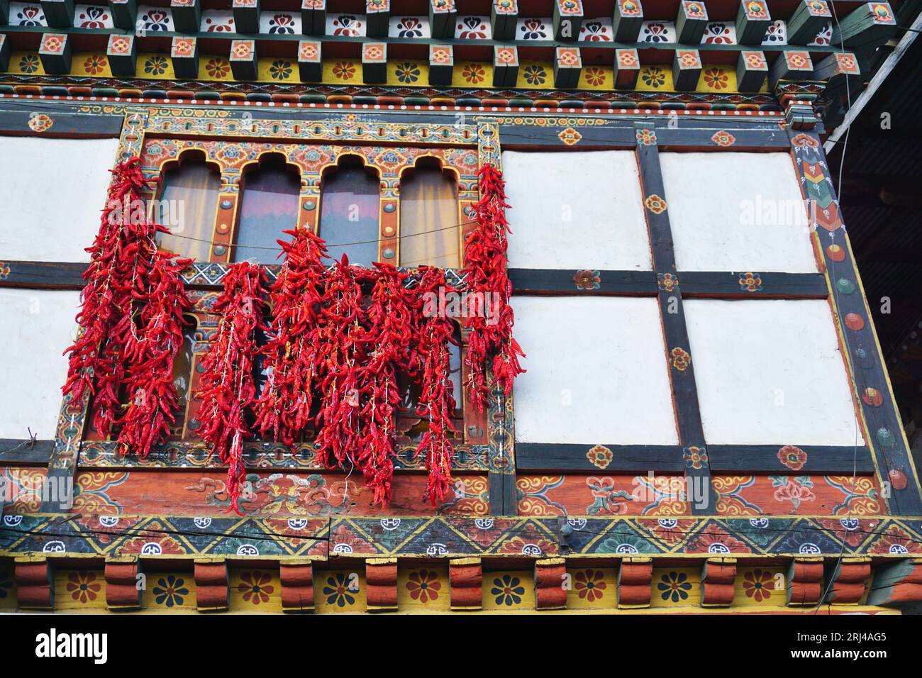 Strings of bright red hot chili peppers hanging to dry from traditional colorful painted wood Bhutanese rabsel window frames in Paro, Bhutan. Stock Photo