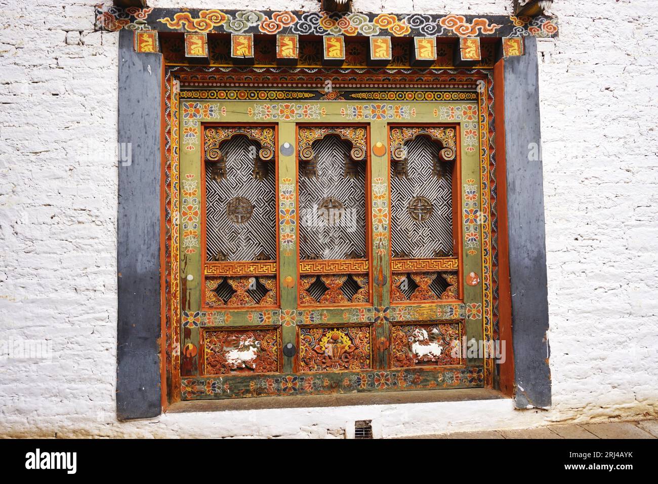 Detail of traditional decorative carved, painted wooden panels with heavy timber frame, set in white stone wall at Punakha Dzong, Kingdom of Bhutan Stock Photo