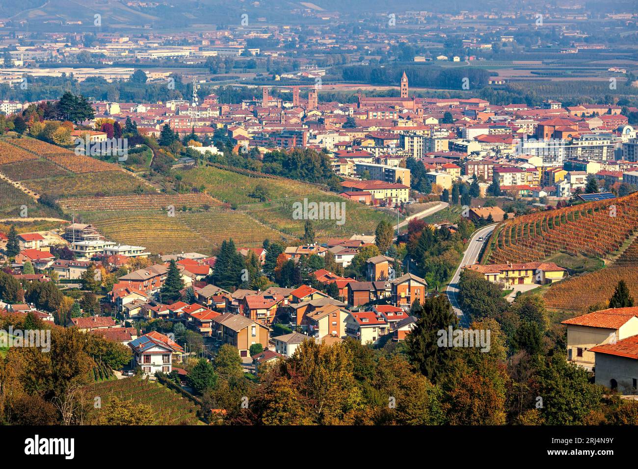 View from above of the hills with autumnal vineyards and the town of Alba in Piedmont, Italy. Stock Photo