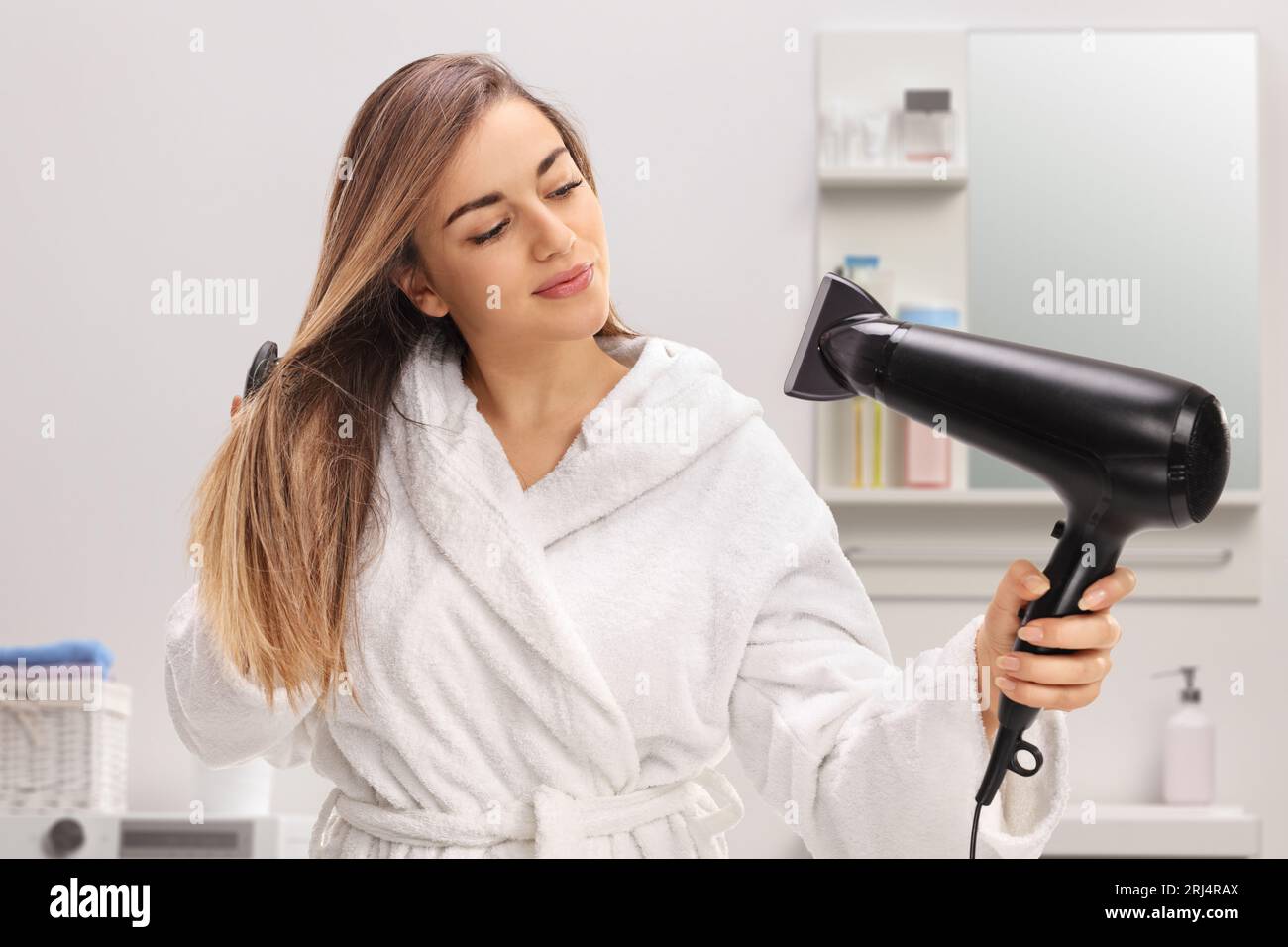Girl in a bathrobe blowing her hair with a hairdryer at a bathroom