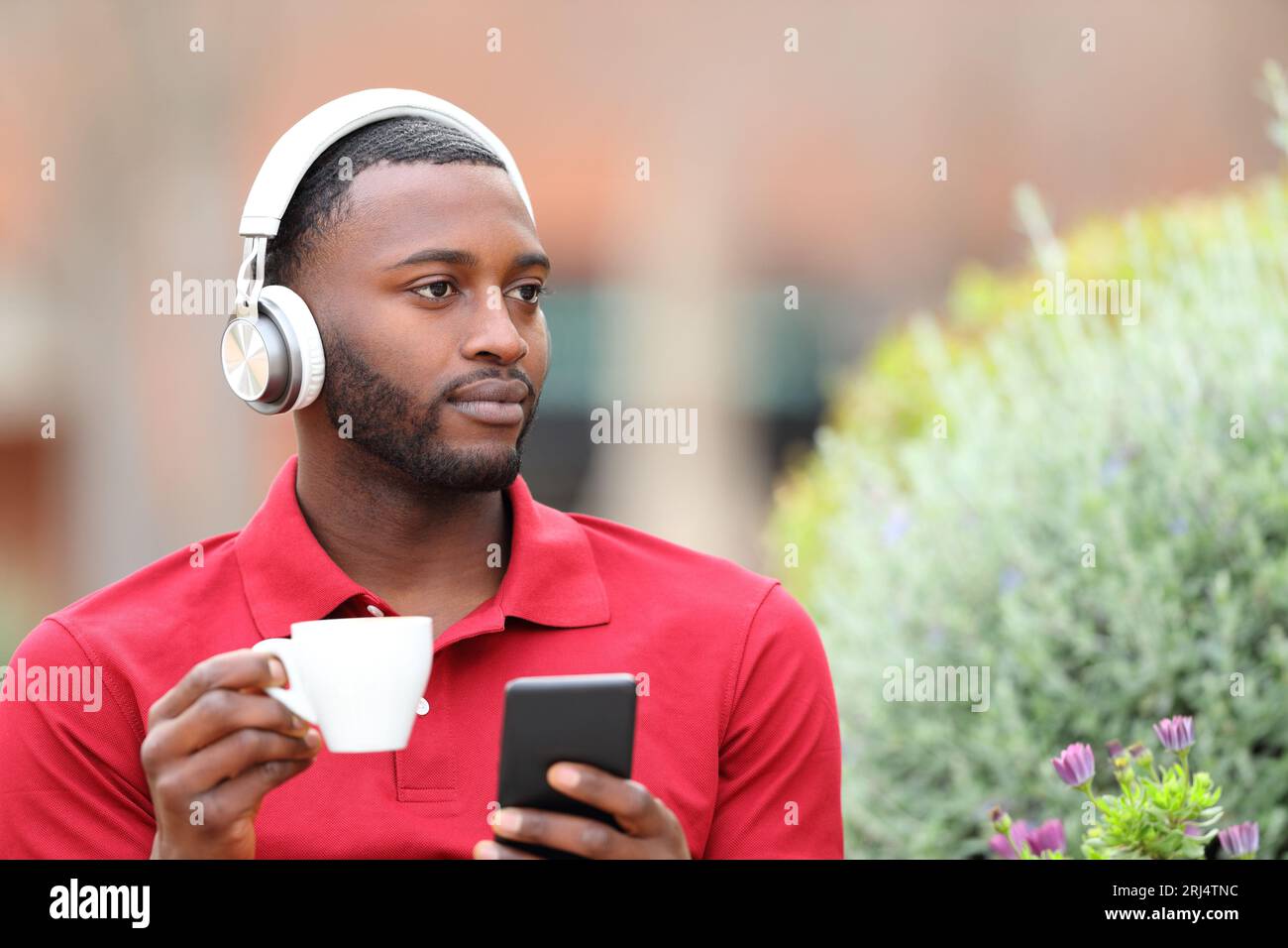 Black man listening to music from headphones holding phone and drinking