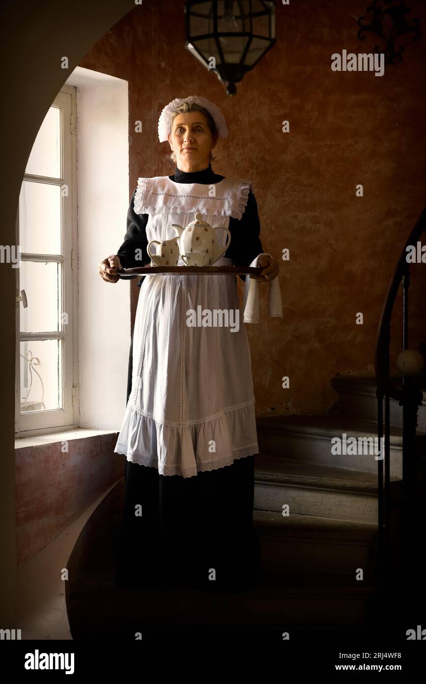Victorian maid or servant in black dress, lace cap and white apron working in a 19th century interior Stock Photo