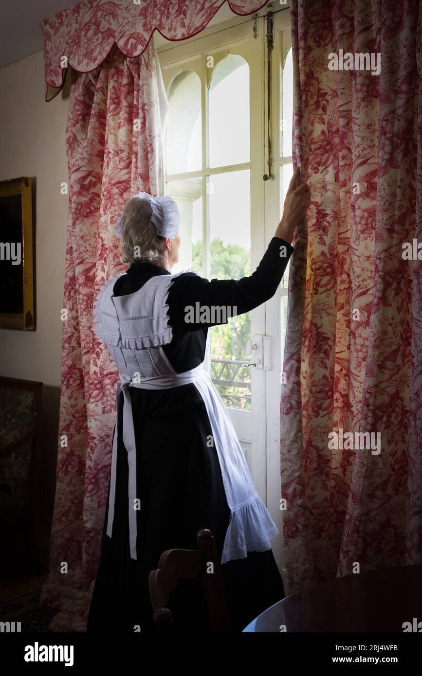 Victorian maid or servant in black dress, lace cap and white apron working in a 19th century interior Stock Photo