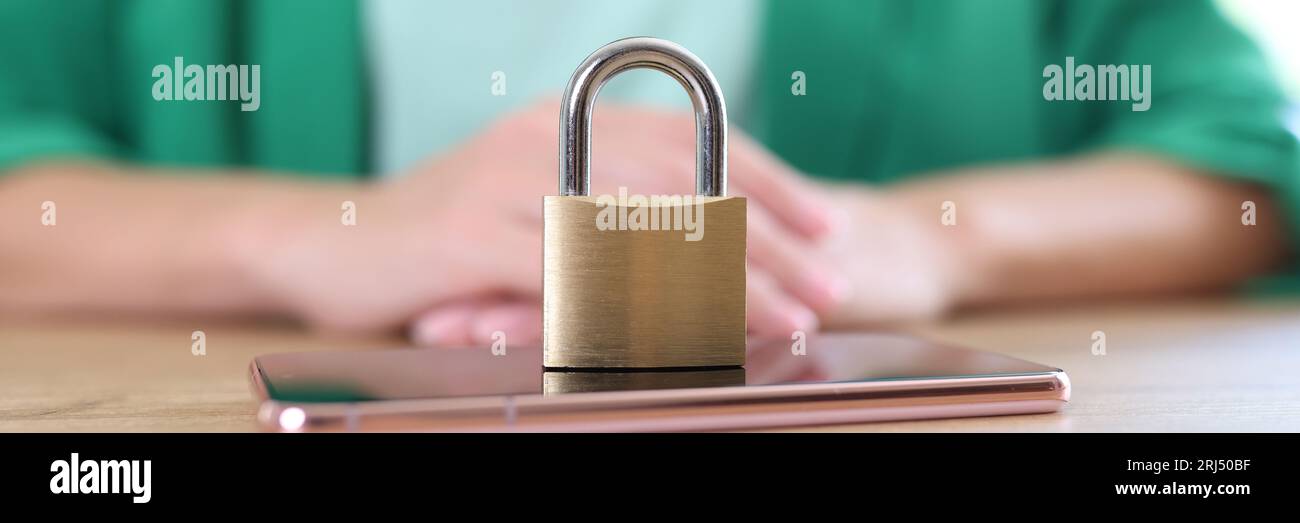 Metal padlock and mobile phone on wooden table close-up, woman in background. Smartphone data protection and information privacy concept. Stock Photo
