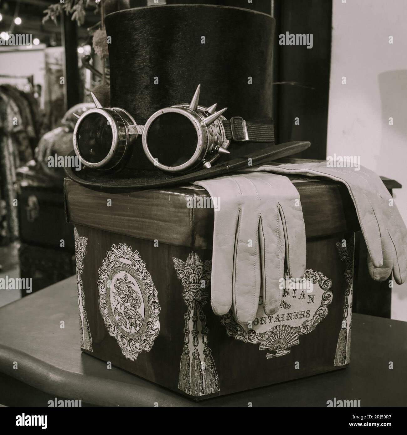 Black top hat with steampunk style sunglasses atop of a pair of leather gloves perched on a decorative box. Stock Photo