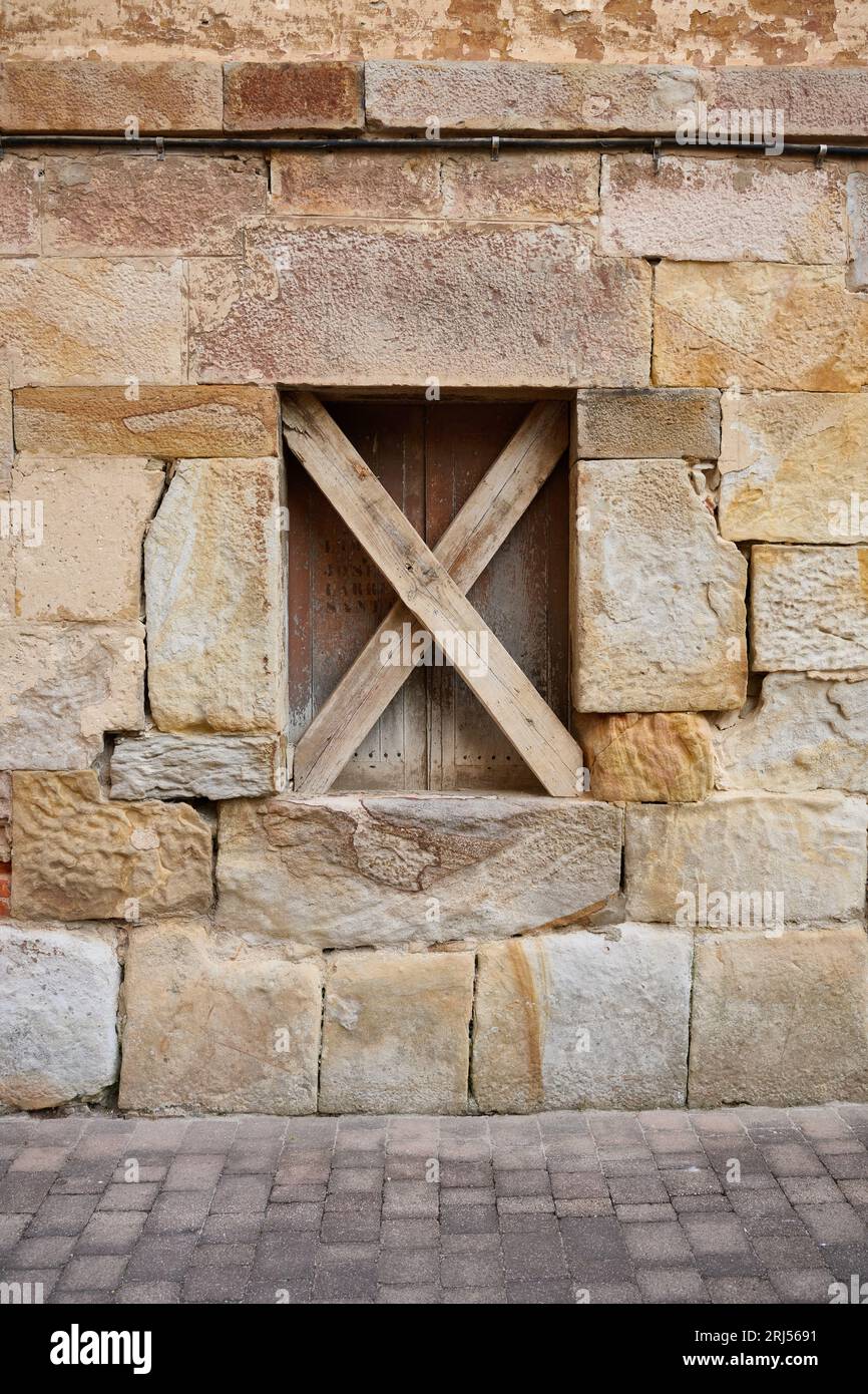 Close up view of stone facade with wooden window blocked with two x-shaped wooden slats Stock Photo
