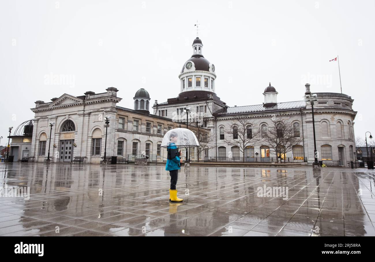 Small boy wearing rain gear holding umbrella in a rainy city square. Stock Photo