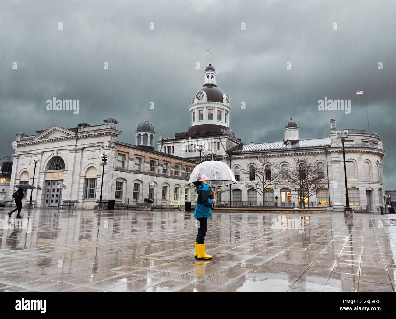Young boy looking up at stormy sky through a clear umbrella in a city. Stock Photo