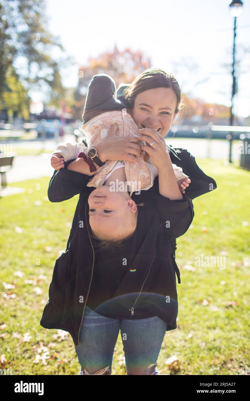 A young mother playfully holds her toddler daughter upside down. Stock Photo