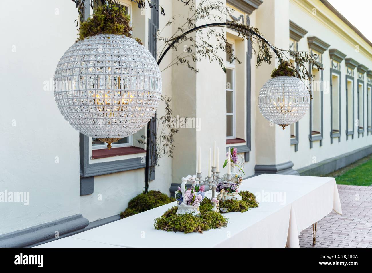 A festive table decorated with a floral arrangement with bouquets of flowers, candles and green moss in the courtyard of the estate under crystal chan Stock Photo