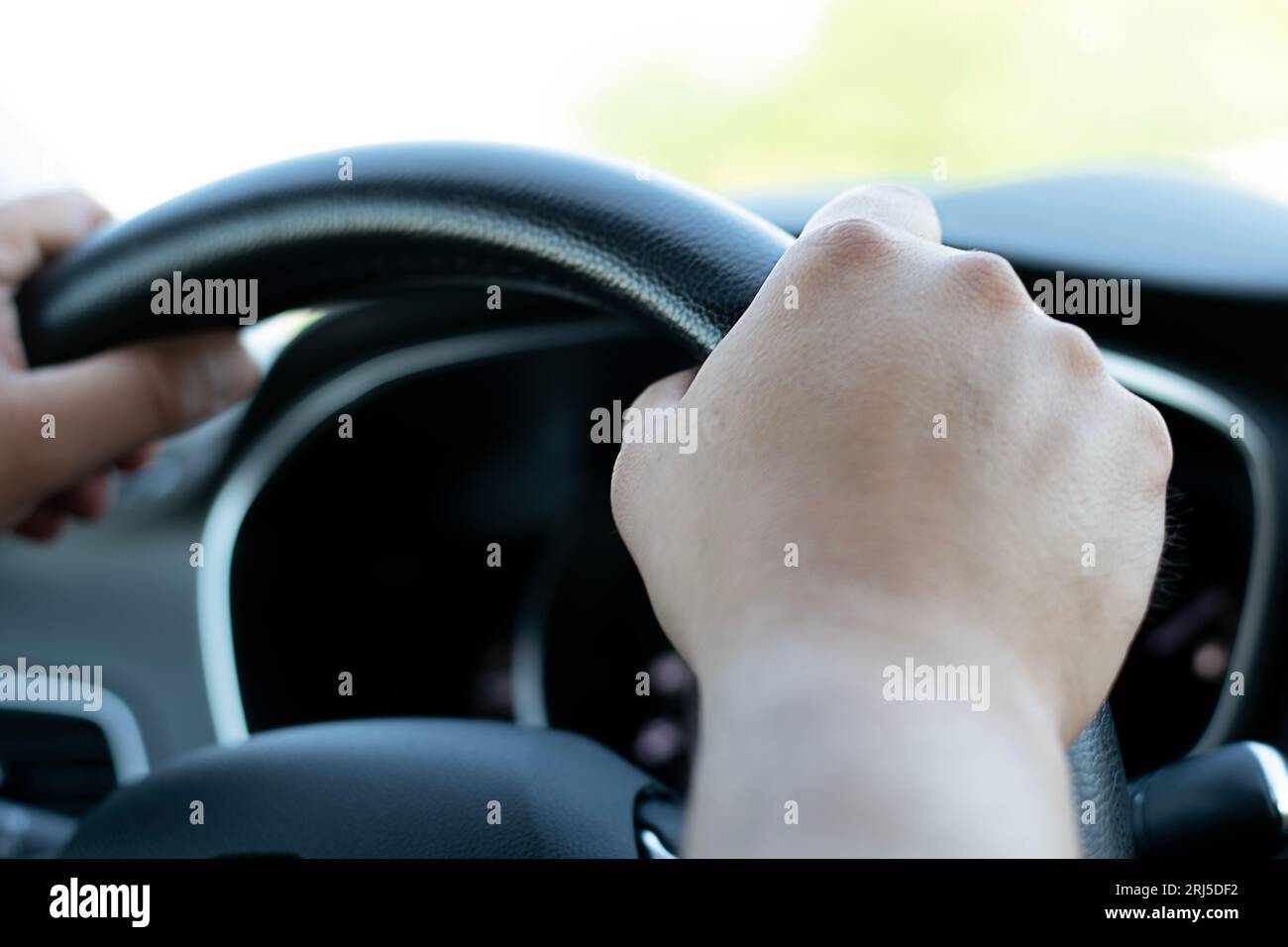 Male hands firmly hold the black steering wheel of a car. The driver