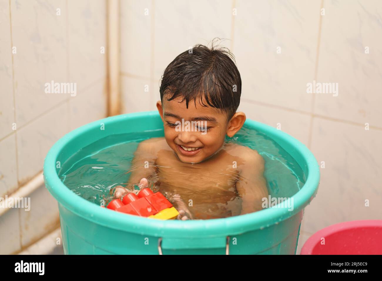 A cheerful South Asian young boy playing in a bathtub filled with water