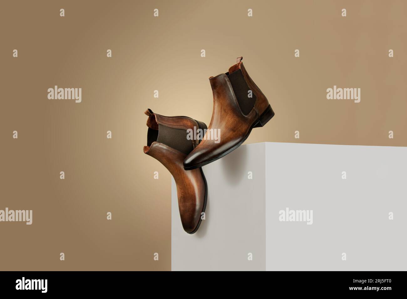 A pair of brown leather boots on a white platform about to fall. Stock Photo