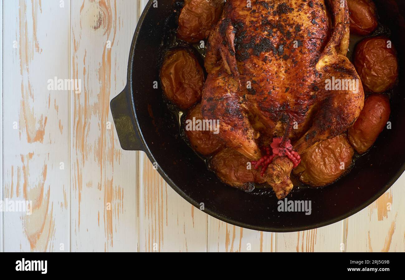 Oven-roasted baked chicken with apples in cast iron skillet pan on the white wooden background food photo tabletop, flat lay view. Stock Photo