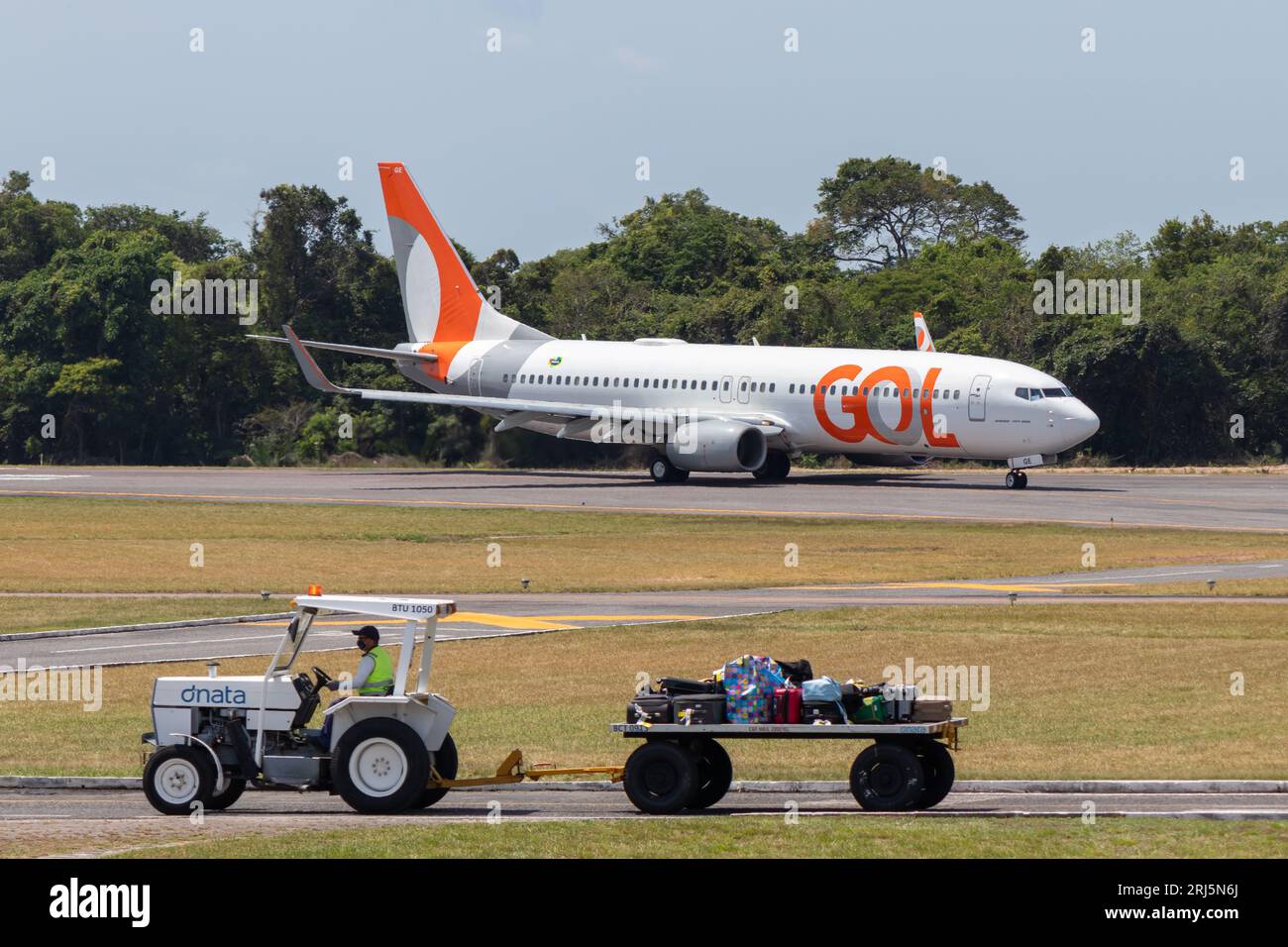 Baggage transport tractor at Santarem Airport (SBSN) with a GOL Airlines plane in the background. Stock Photo