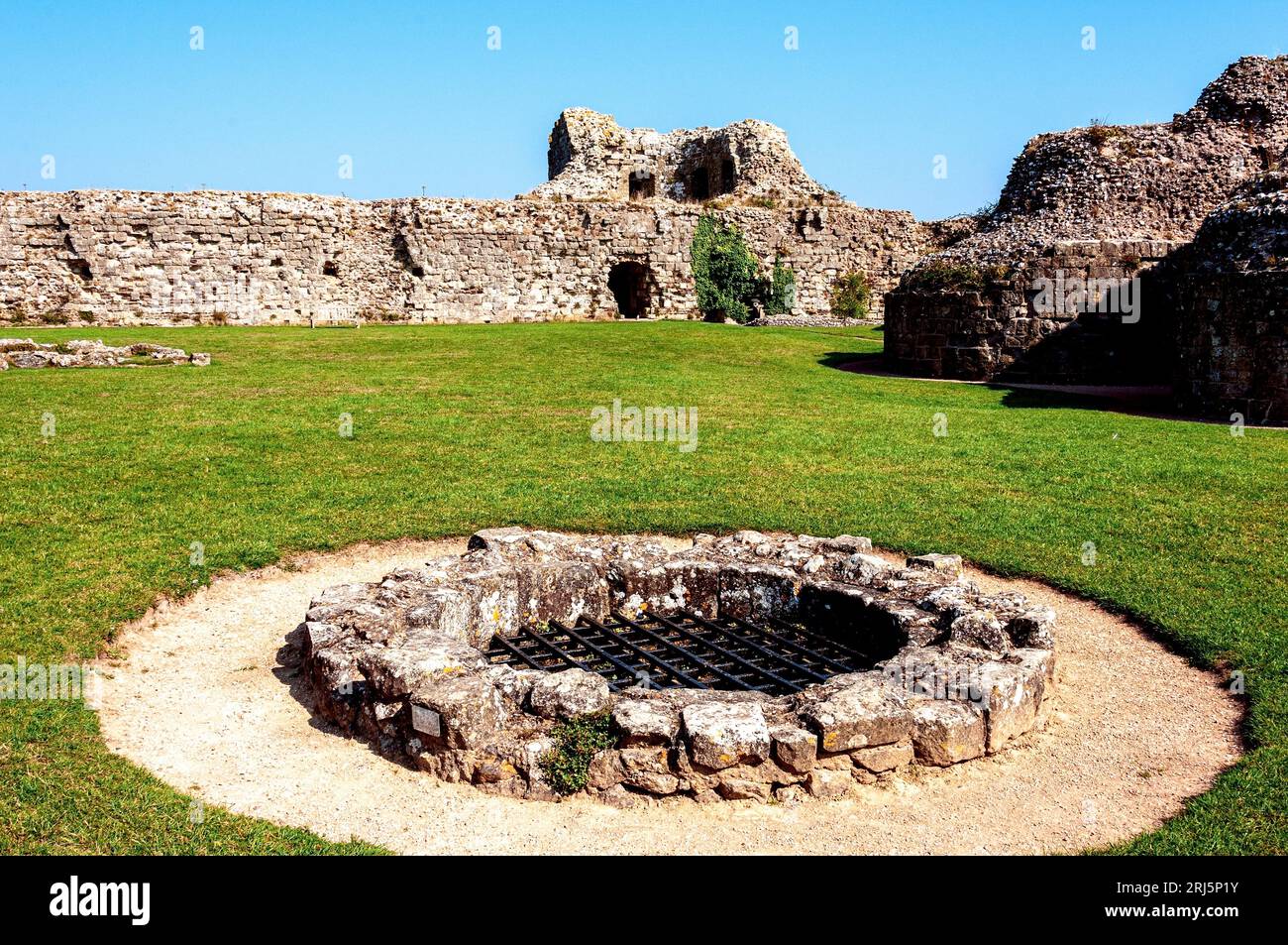 The well fitted with an iron grid at the top inside the inner bailey of Pevensey Castle and close to a bastion of the keep and the the curtain walls Stock Photo