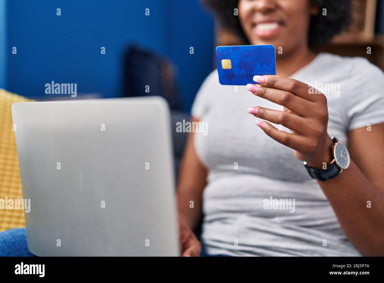 African american woman using laptop and credit card sitting on sofa at ...