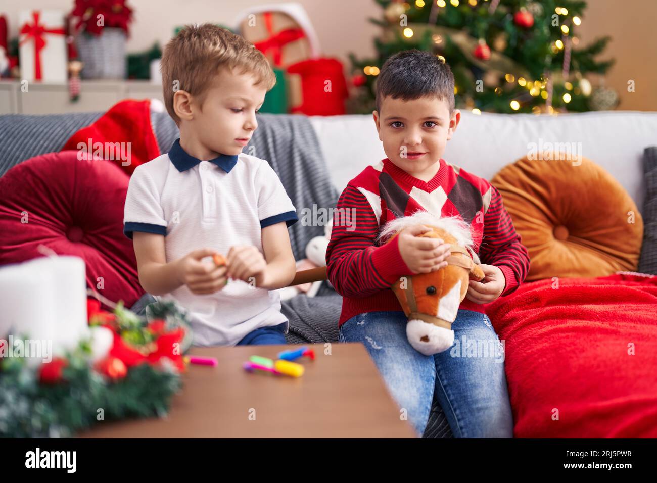 Two kids playing with toys sitting on sofa by christmas tree at home Stock Photo