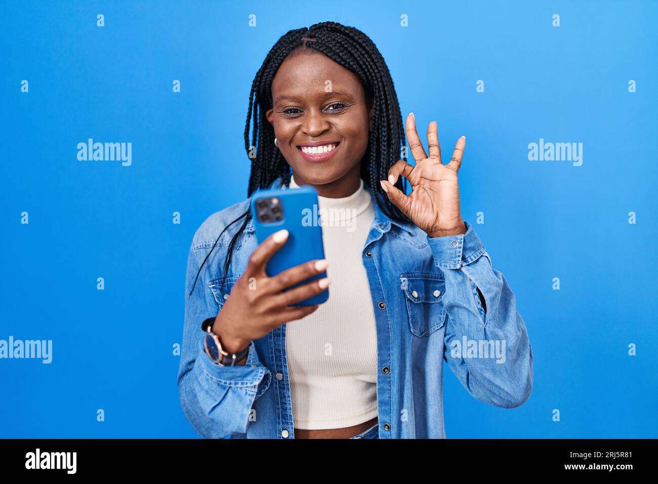 African woman with braids using smartphone typing message doing ok sign ...