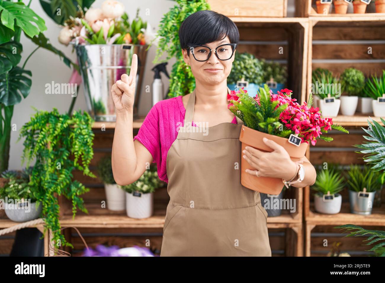 Young asian woman with short hair working at florist shop holding plant ...