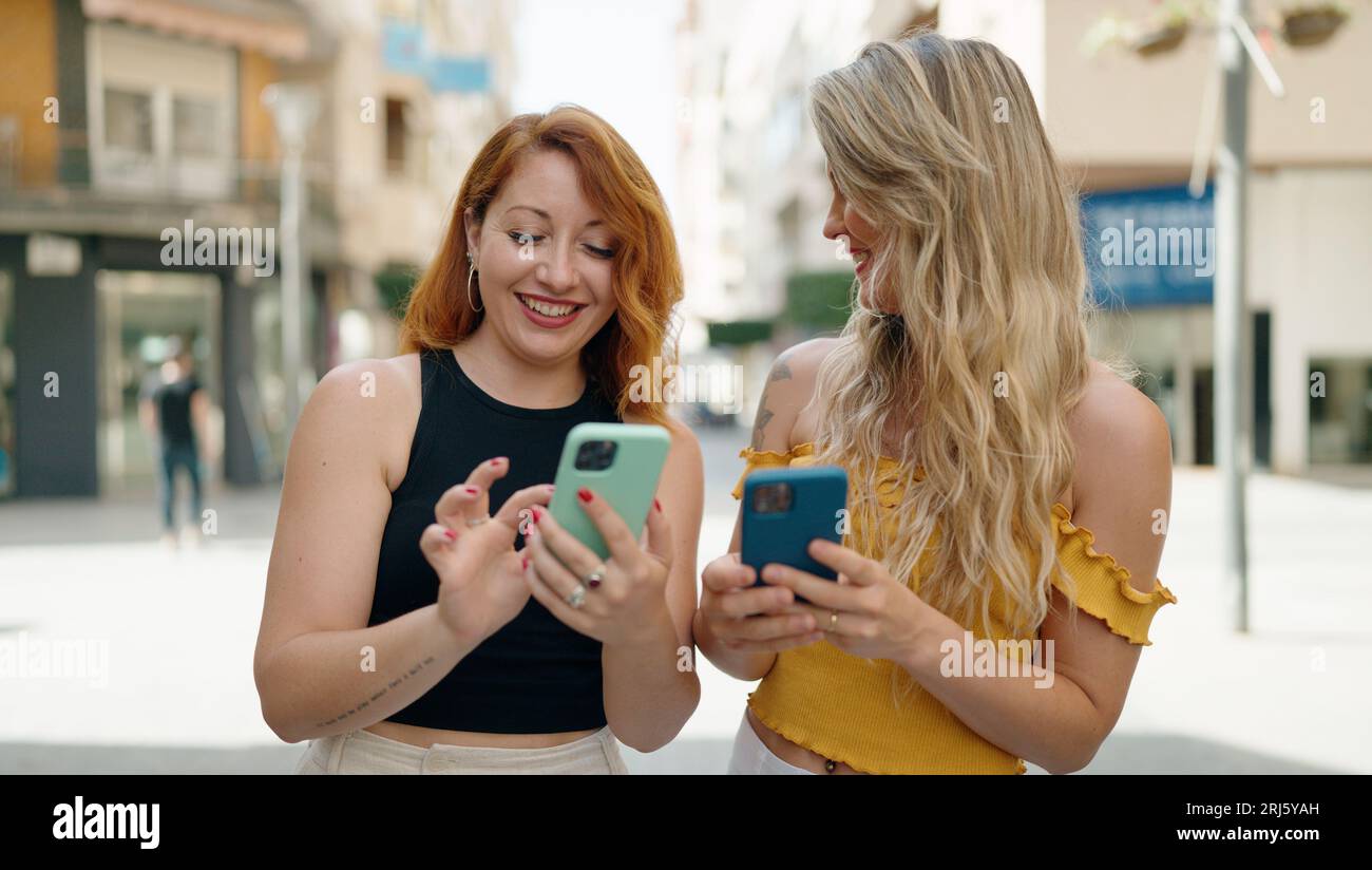 Two women standing together using smartphones at street Stock Photo - Alamy
