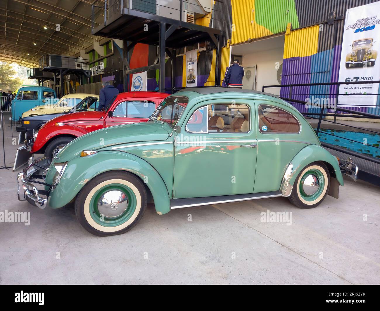 Old green popular Volkswagen Type 1 Beetle or Bug sedan, air cooled, rear engine, in a colorful warehouse yard. Expo Fierro 2023 classic car show Stock Photo