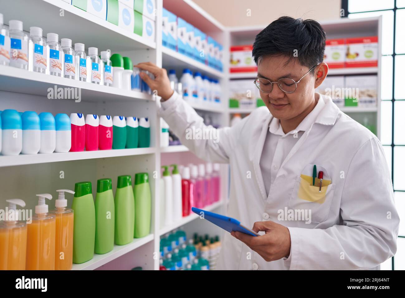 Young chinese man pharmacist using touchpad working at pharmacy Stock ...