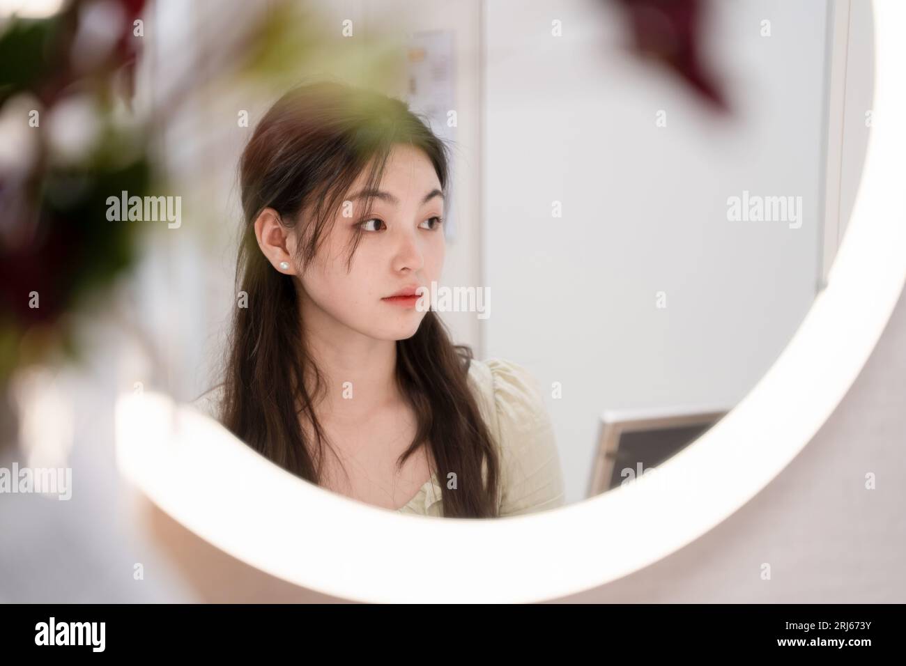 An East Asian female looking at her reflection in a large mirror in a ...