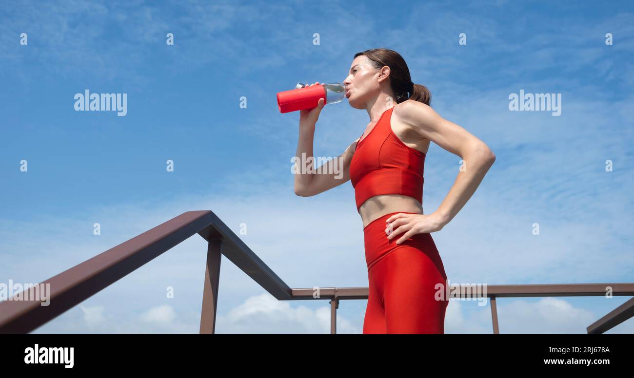 Fit, sporty woman drinking water after exercise or running in the heat. Outdoor fitness concept. Stock Photo
